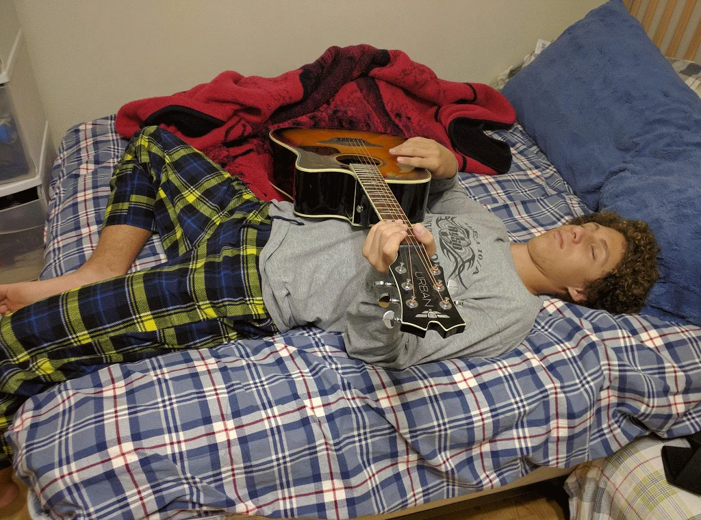 High-school Joey asleep holding a guitar; when it’s removed, his hands stay in playing position